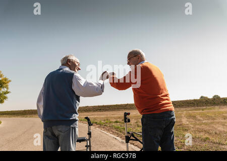 Two old friends with wheeled walkers, greeting in the street Stock Photo