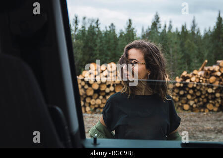Young woman standing beside car next to stack of wood Stock Photo