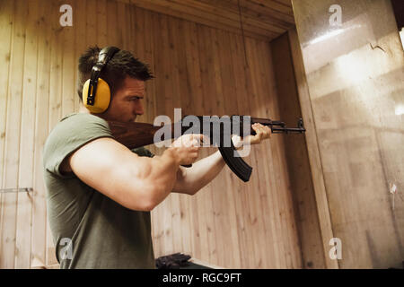 Man aiming with a rifle in an indoor shooting range Stock Photo