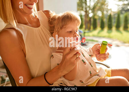 Happy mother and daughter blowing soap bubbles on porch Stock Photo