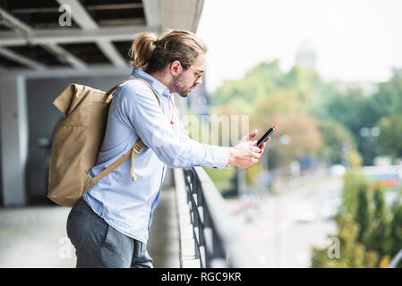 Young businessman with backpack, standing in parking garage, using smartphone Stock Photo