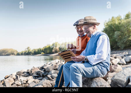 Two old friends sitting by the riverside, using digital tablet Stock Photo