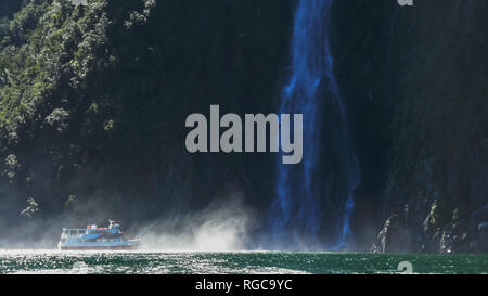 a cruise boat sails into the spray at the base of stirling falls in milford sound, new zealand Stock Photo
