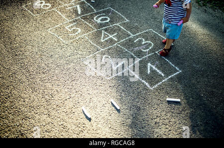 Little girl with drawn hopscotch on the street, partial view Stock Photo