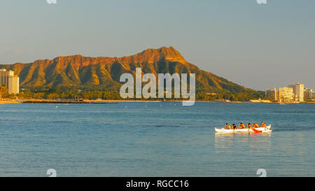 a crew of boys paddle an outrigger canoe at waikiki beach with diamond head in the distance Stock Photo