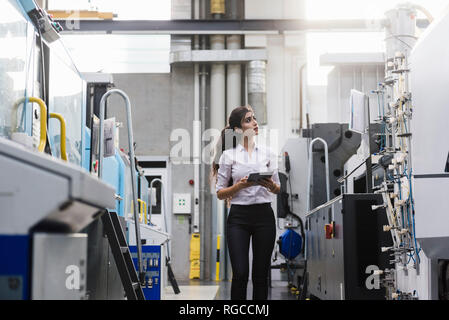 Woman with tablet at machine in factory shop floor lookig around Stock Photo