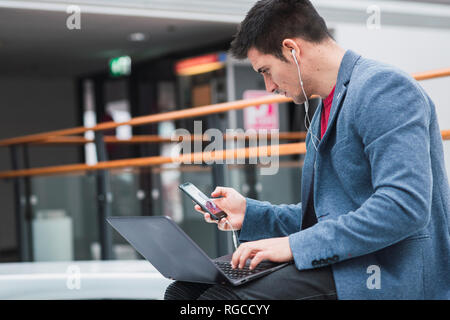 Businessman in lobby of a modern building, using smartphone and laptop Stock Photo