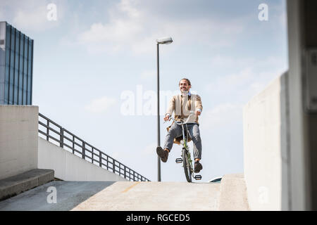 Laughing businessman riding down a ramp on his bicycle Stock Photo