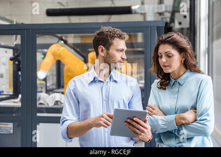 Colleagues in high tech company controlling industrial robots, using digital tablet Stock Photo