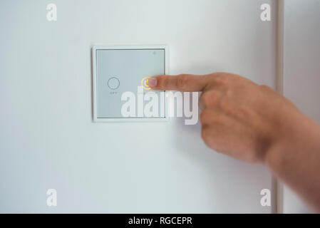 Woman using smart home switch on wall Stock Photo