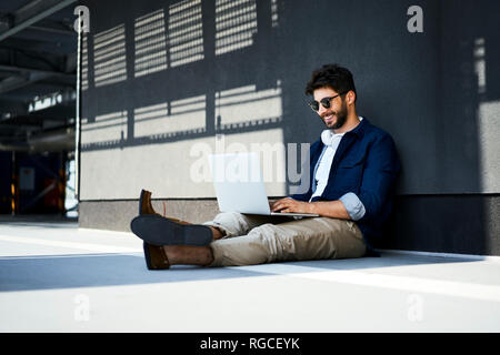Relaxed young man sitting on the ground using laptop Stock Photo