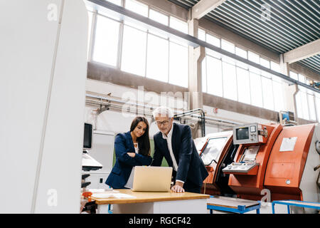 Businessman an woman in high tech enterprise, having a meeting, using laptop Stock Photo