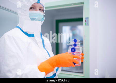 Lab technician wearing cleanroom overall holding containers at material sluice