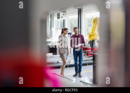 Businessman and woman having a meeting in front of industrial robots in a high tech company Stock Photo