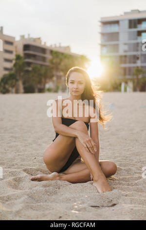 Portrait of beautiful young woman sitting on the beach at sunset Stock Photo