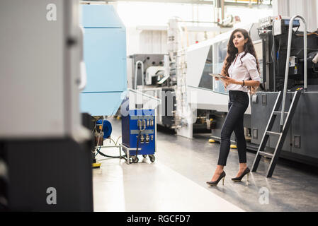 Woman with tablet at machine in factory shop floor looking around Stock Photo