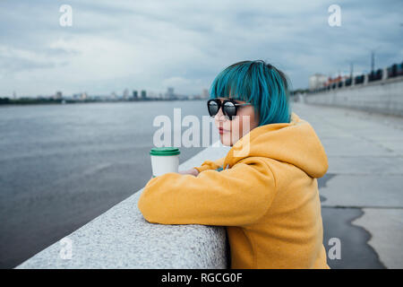 Young woman with dyed blue hair leaning on a wall looking at distance Stock Photo