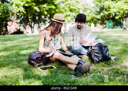 Two students sitting on a meadow in a park looking at notes Stock Photo