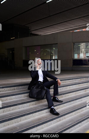 Stylish senior businessman on the phone sitting on stairs outdoors Stock Photo