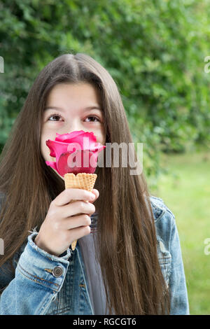 Girl smelling pink rose blossom in ice cream cone Stock Photo