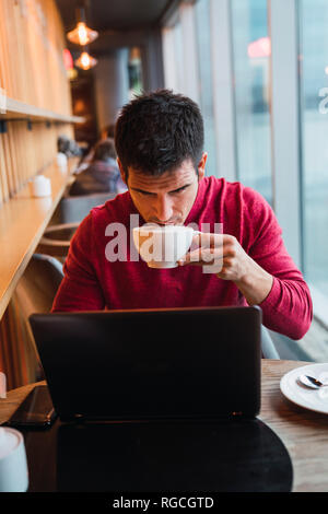Businessman sitting in a restaurant using laptop, drinking coffee Stock Photo