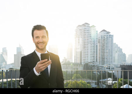 Business man in dark suit with smartphone on city rooftop Stock Photo