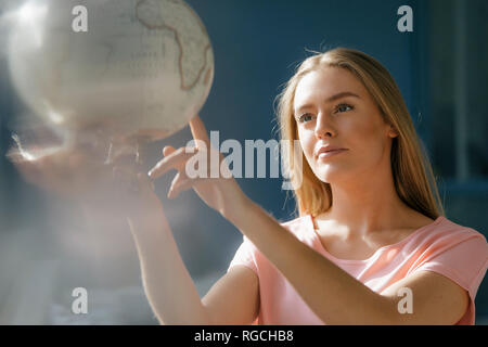 Portrait of young woman looking and pointing at globe Stock Photo