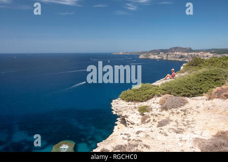 Corsica, Mediterranean coast, woman sitting on rocky cliff Stock Photo