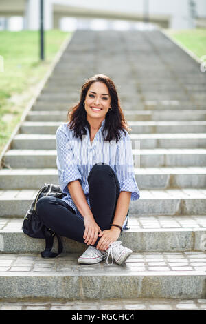 Portrait of smiling student sitting on stairs outdoors Stock Photo