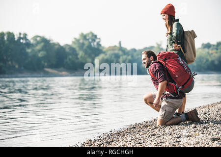 Smiling young couple with backpacks at the riverside Stock Photo