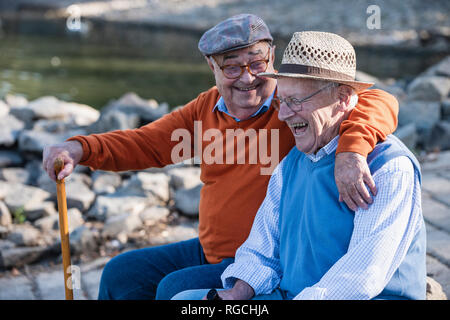 Two old friends sitting by the riverside, having fun Stock Photo