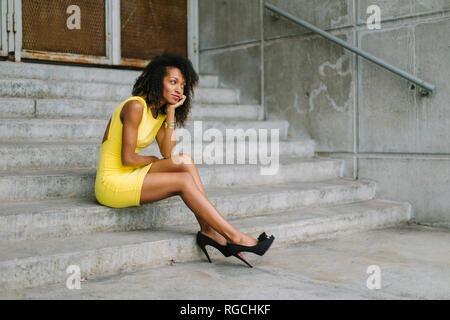Fashionable businesswoman in yellow dress and high heels sitting on stairs Stock Photo