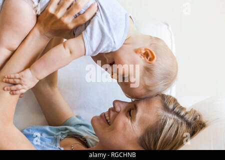 Happy mother cuddling with her baby girl on couch Stock Photo