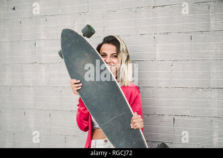 Portrait of a young woman with her long board, in front of a wall Stock Photo
