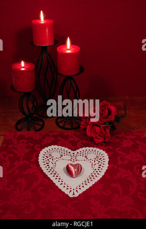 Heart shapped dollie and gemstone, three red candles in metal holoders and bouquet of red roses on wooden table. Stock Photo