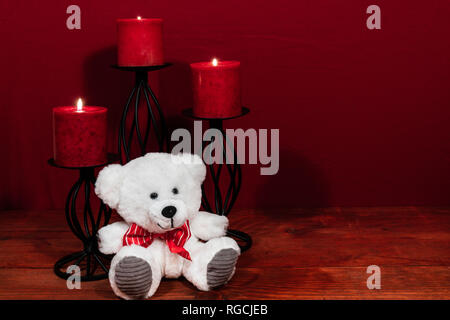 Three red candles in metal holders and red rose, one teddy bear on wooden table. Stock Photo