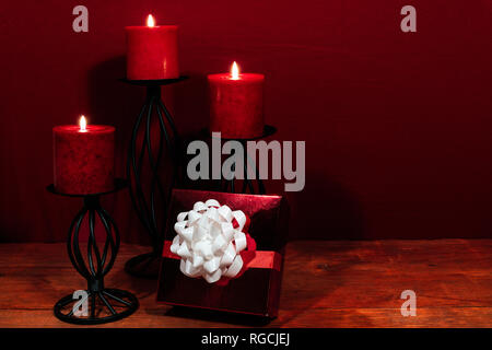 Three red candles in metal holders and red rose, present with white bow on wooden table. Stock Photo