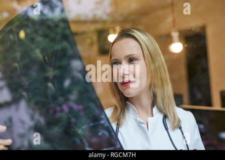 Female doctor looking at x-ray image behind windowpane Stock Photo
