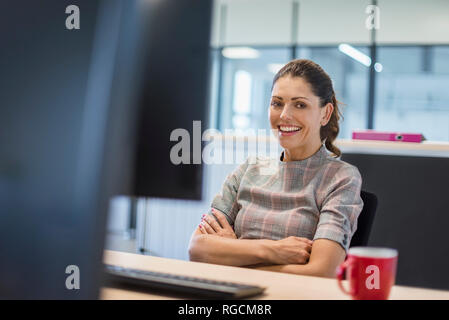 Female office worker sitting at desk, with arms crossed Stock Photo