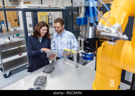 Colleagues in high tech company controlling industrial robots, using digital tablet Stock Photo