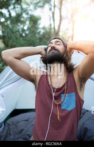 Portrait of man in front of tent listening music with earphones Stock Photo