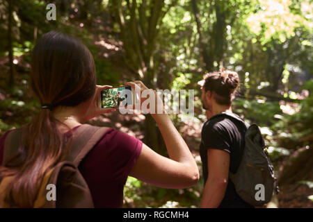 Spain, Canary Islands, La Palma, woman taking a cell phone picture of her boyfriend in a forest Stock Photo