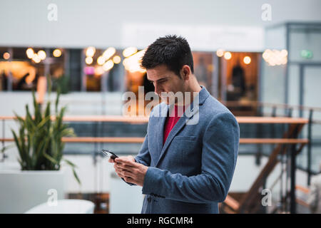 Businessman in lobby of a modern building, using smartphone Stock Photo