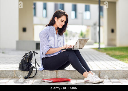 Content student sitting on stair outdoors working on laptop Stock Photo