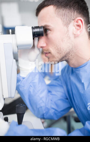 Lab technician looking through microscope Stock Photo