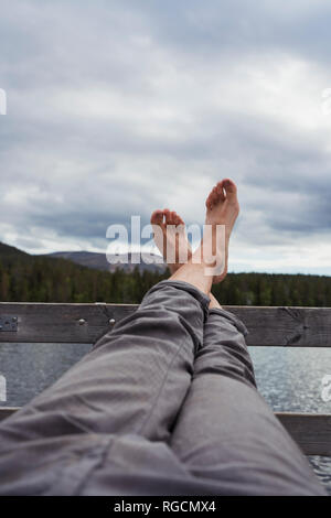 Man sitting on jetty at a lake holding his feet up Stock Photo