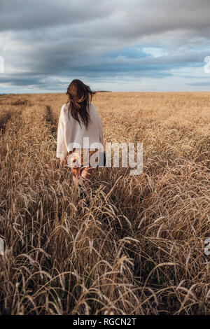 Back view of young woman walking in corn field Stock Photo