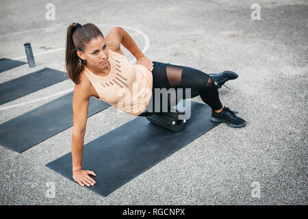 Young woman doing side plank exercise with fascia roll outdoors Stock Photo