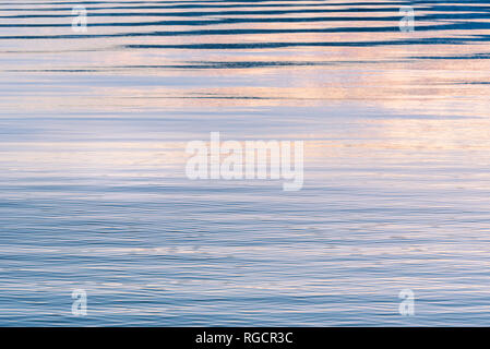 Gentle ripples on surface of lake reflecting pink, purple, and blue colors in sky at sunset Stock Photo