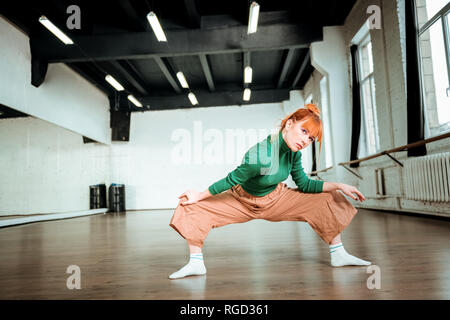 Good-looking slim yoga coach in a green turtleneck doing asana for strong legs Stock Photo